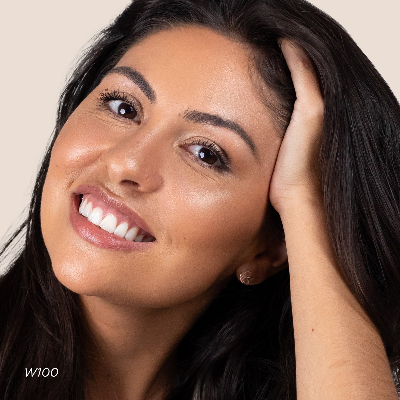 Woman with dark hair smiling and touching her hair against a neutral background