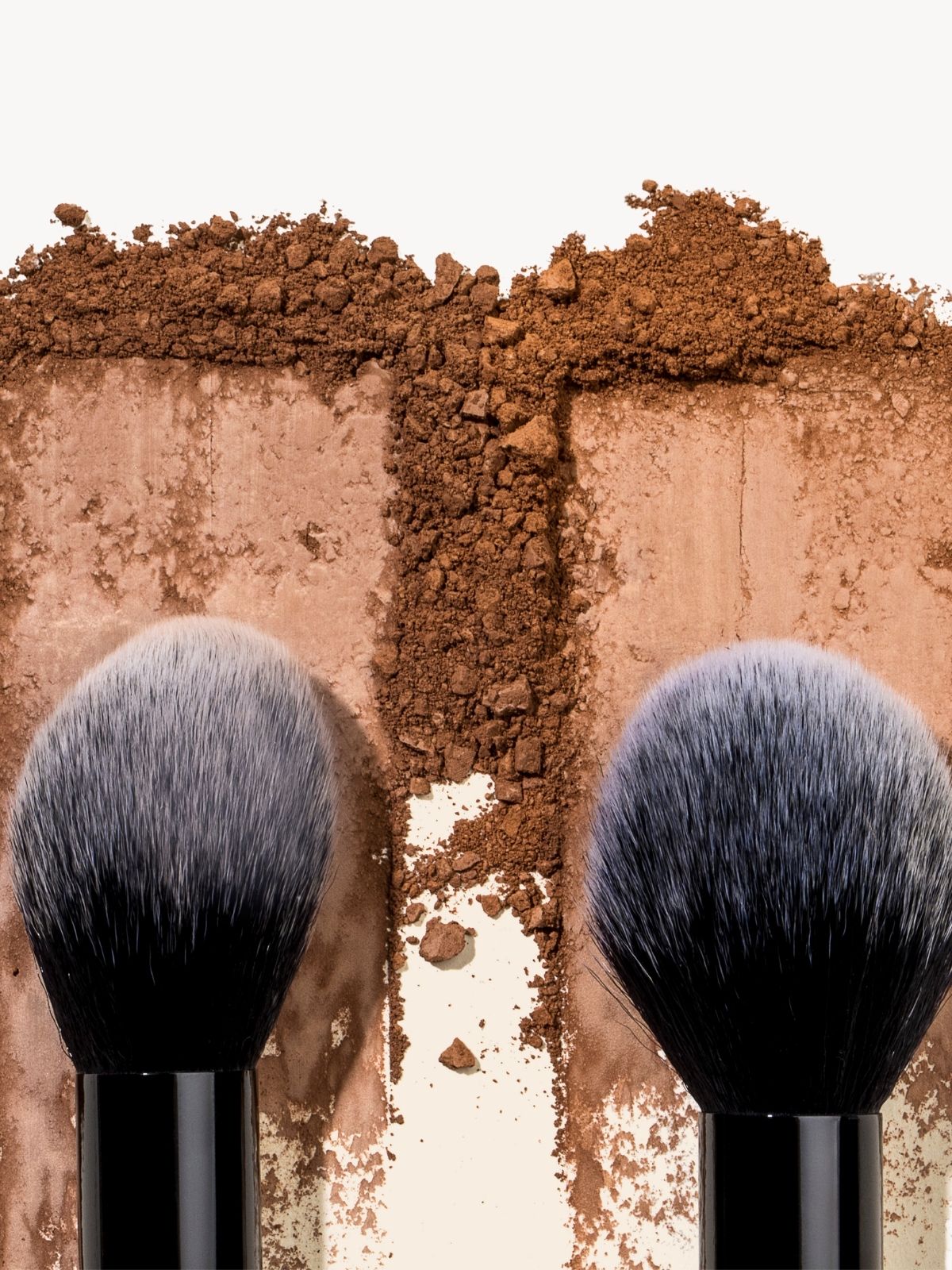 Two makeup brushes with brown powder on a white background