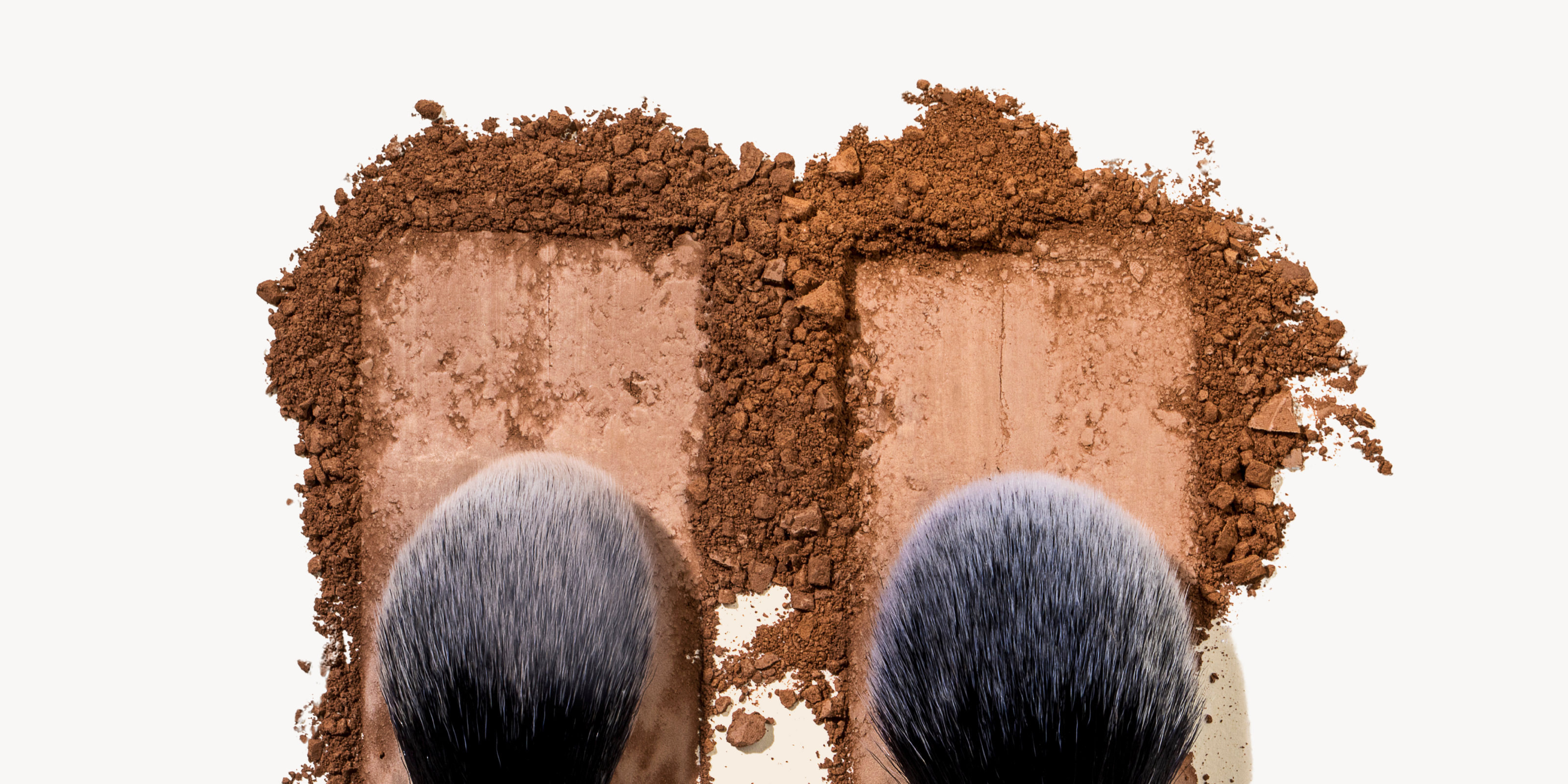 Makeup palette with three shades of brown and two brushes on a white background